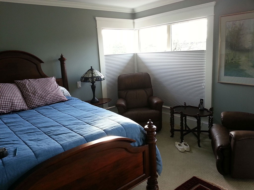 soft white shades covering the bottom portion of a large corner bedroom window white letting light in the top