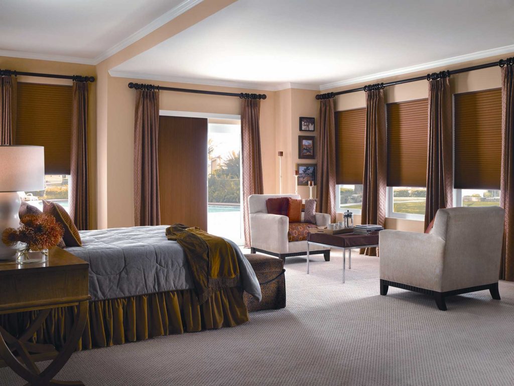 A bedroom with matching brow horizontal shades on the windows and vertical shades on the patio doors